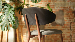 Detail of a dark wooden Mobitec Toro chair with grey seat by a brick wall