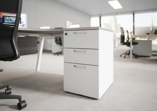 Lifestyle image of a white Buronomic Comfort desk-height pedestal next to a desk in an open office