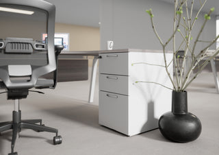 Lifestyle image of a white Buronomic Comfort desk-height pedestal next to a black vase